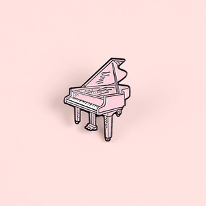 Broche en émail piano rose avec détails de clavier noir sur fond rose pastel doux