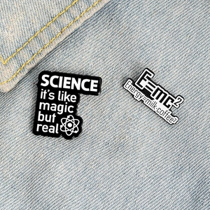 Creative Science enamel pins with E=mc2 and atomic designs on blue denim background