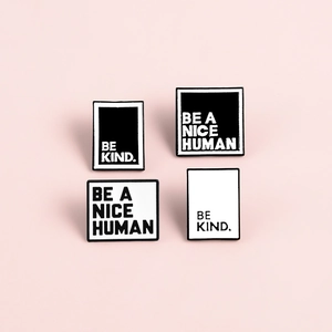 Minimalist BE A NICE HUMAN and BE KIND enamel pins set in black and white on pink backdrop