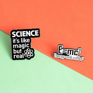 Close-up of creative science enamel pins featuring E=mc² and physics themes on split background