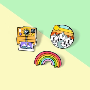 Set of three creative enamel pins featuring camera, rainbow, and mountain sunset designs