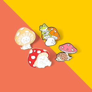 Macro shot of cute cartoon cat, frog, and hedgehog mushroom enamel pins with gold trim