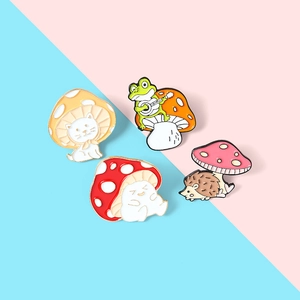 Detailed view of four colorful enamel mushroom pins featuring a cat, frog, and hedgehog