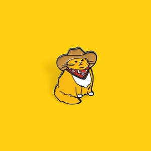 Cartoon orange cowboy cat enamel pin featuring a brown hat and red bandana on yellow background