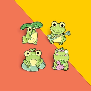 Detailed view of four cute green enamel pins featuring frogs with guitar and strawberry