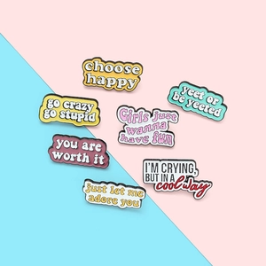 Gros plan de sept pin's colorés en émail avec citations de motivation sur un fond bicolore chic