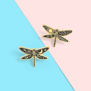 Detailed close-up of dragonfly enamel pins with celestial gold sun and moon patterns
