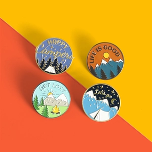 Close-up of four round camping enamel pins with mountain and tent landscape designs