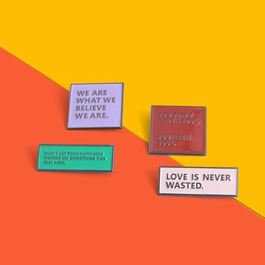 Close-up of four colorful enamel pins with motivational quotes on a split bright background