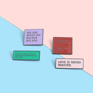 Detailed view of colorful enamel pins with inspirational phrases on pink and blue background
