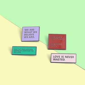 Close-up of four colorful enamel lapel pins with inspirational quotes on bicolor background