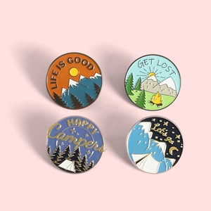 Detail of four enamel outdoor camping pins featuring mountains and forest scenes