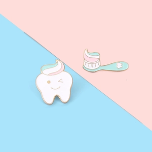 Close-up of creative white tooth and mint green toothbrush enamel pins with gold trim