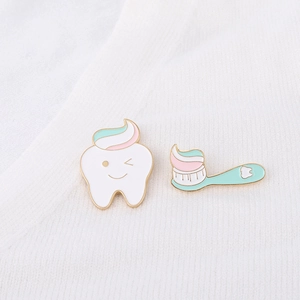 Close-up of cute cartoon enamel pins featuring a smiling white tooth and a mint green toothbrush