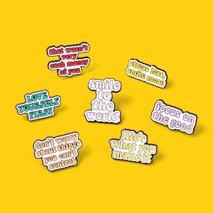 Detailed view of seven colorful enamel pins with motivational quotes on a yellow background