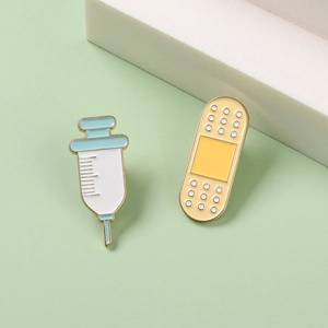 Syringe and bandage enamel pins in blue and yellow colors on a pale green background