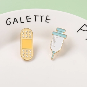 Cartoon medical enamel pin set with yellow bandage and blue syringe on a white plate