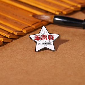 Detail of star-shaped enamel pin with La Jeunesse text on vintage bamboo background