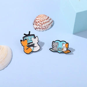 Detail of two cute animal enamel pins featuring fox and cat scenes on a blue background