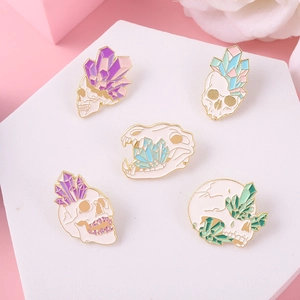 Detail showing five skull and crystal enamel pins on a white hexagonal display stand