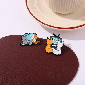 Close-up of enamel pins showing a cute fox watching TV and cats on a blue heart background