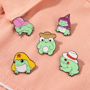 Détail de cinq épinglettes en émail grenouille avec chapeaux colorés sur denim rose
