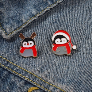 Christmas penguin enamel pins with antlers and santa hat on blue denim background