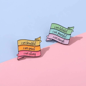 Detail of colorful enamel ribbon brooches with motivational phrases like I am strong