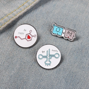 Detailed view of scientific chemistry enamel pins on denim fabric showing OMG and Be Happy motifs