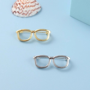 Detail of minimalist eyewear-shaped metal pins in gold and silver on a blue background