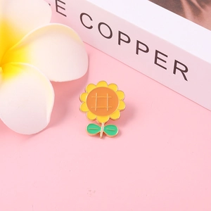 Enamel sunflower brooch with yellow petals and green leaves on a soft pink background