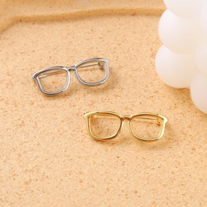 Creative gold and silver metal eyeglasses frame pins on a cork background surface