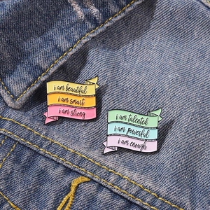 Detail of rainbow ribbon enamel pins with motivational quotes pinned on blue denim fabric