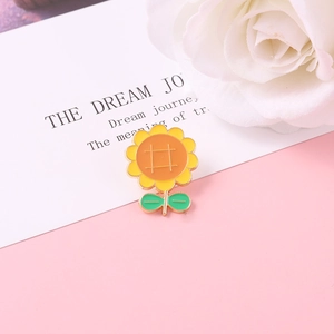 Cute sunflower enamel pin with vibrant yellow petals and green leaves on a pink surface