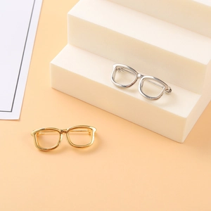 Pair of creative gold and silver spectacle pins displayed on a minimalist tiered stand
