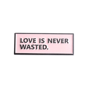 Detailed shot of pink enamel brooch with Love Is Never Wasted slogan and black metal frame