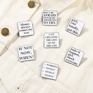 Detailed close-up of square white enamel pins with black motivational quotes on a jacket