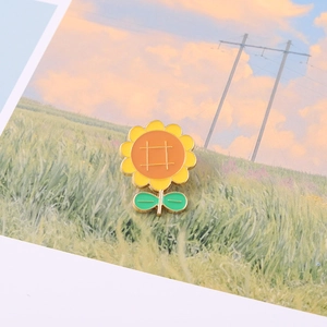 Sunflower enamel brooch pin with yellow petals and green leaves on a landscape card