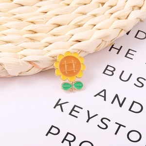 Minimalist sunflower enamel brooch with yellow petals and green leaves on a soft background
