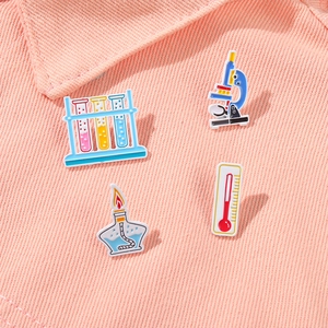 Set of four science enamel pins including microscope and test tubes on pink denim fabric