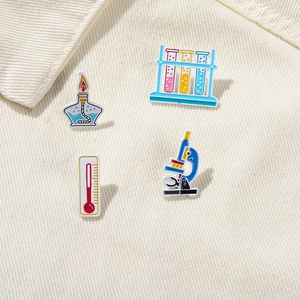 Detailed close-up of science enamel pins set featuring a microscope and test tubes