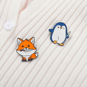 Détail de pins en émail renard et pingouin avec couteaux sur un pull rayé blanc