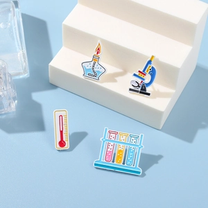 Close-up of lab enamel pins featuring microscope, thermometer, test tubes, and spirit lamp