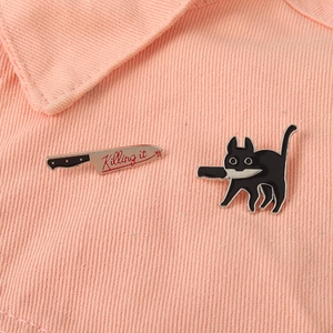 Dettaglio macro del set di spille in smalto gatto nero e coltello su denim