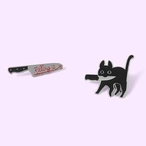 Dettaglio delle spille in smalto con gatto nero con coltello e scritta Killing it