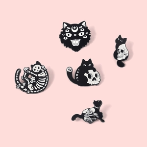 Detailed close-up of 5 gothic black cat enamel pins with skull and moon motifs on pink