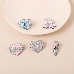 Detailed set of five pastel enamel pins with pink skull and heart motifs on a beige surface
