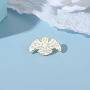 Close-up of owl enamel brooch with white feathers and golden edges on a blue background