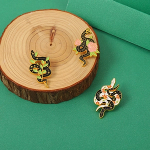 Close-up of three snake enamel pins with floral details on natural wood and green background