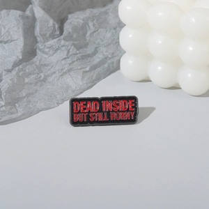 Close-up of rectangular black enamel pin featuring red Dead Inside But Still Horny text